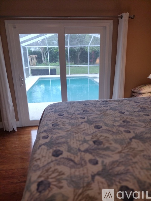 A bedroom with a bed and a pool outside the window.