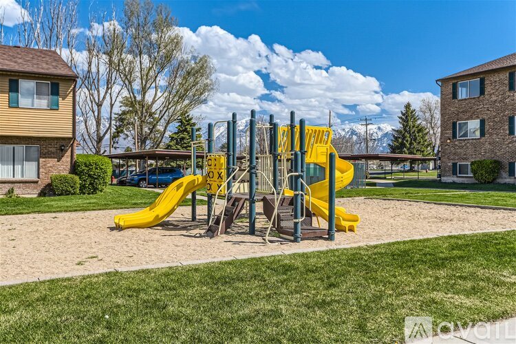 A playground with a yellow slide and a green lawn.