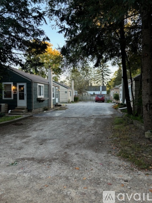 A gravel driveway leads to a row of houses with trees on either side.