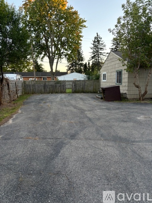 A gravel driveway leads to a house with a fence and trees in the background.