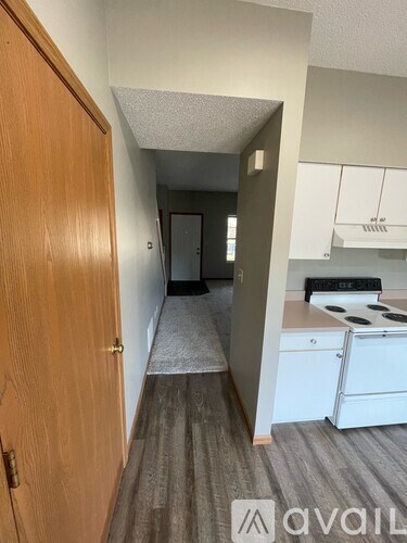 A hallway leads to a kitchen area with white cabinets and a stove.