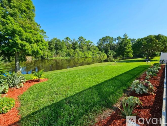 A well-maintained lawn with a pond and trees in the background.