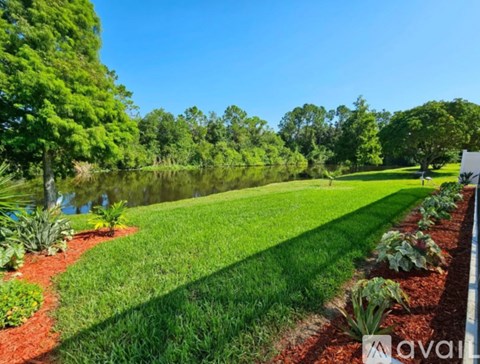 A well-maintained lawn with a pond and trees in the background.