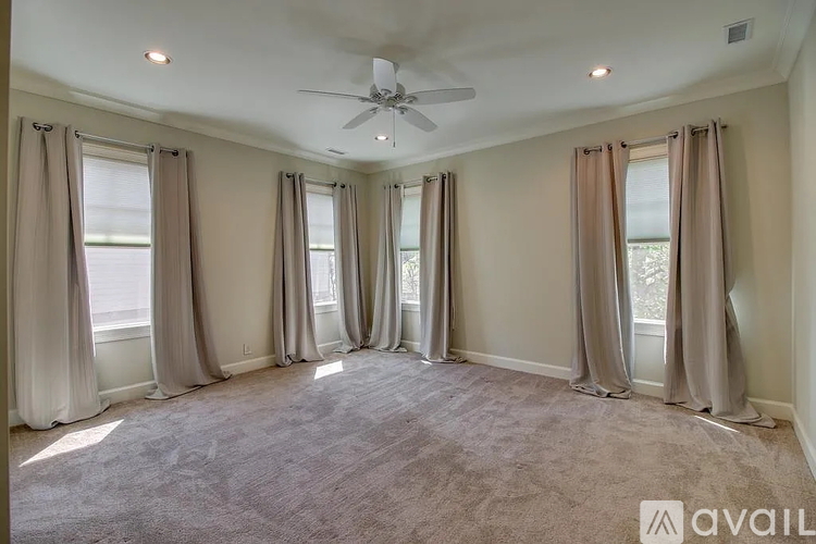 A spacious room with a ceiling fan and large windows with curtains.