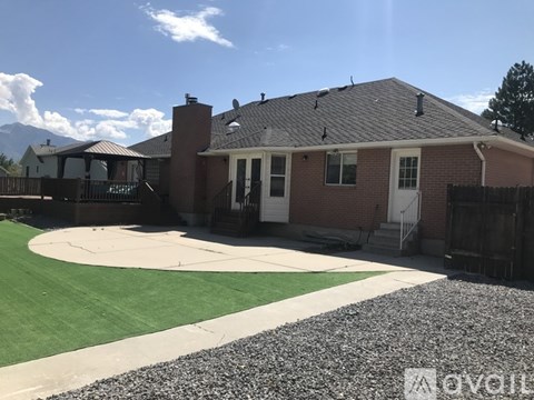 A house with a red brick exterior and a white door is surrounded by a gravel driveway and a green lawn.