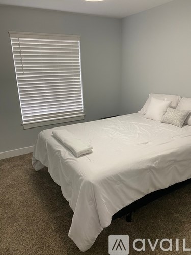 A bedroom with a white bed and a window with blinds.