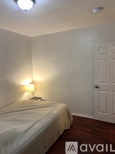 A bedroom with a bed, lamp, and wooden floors.