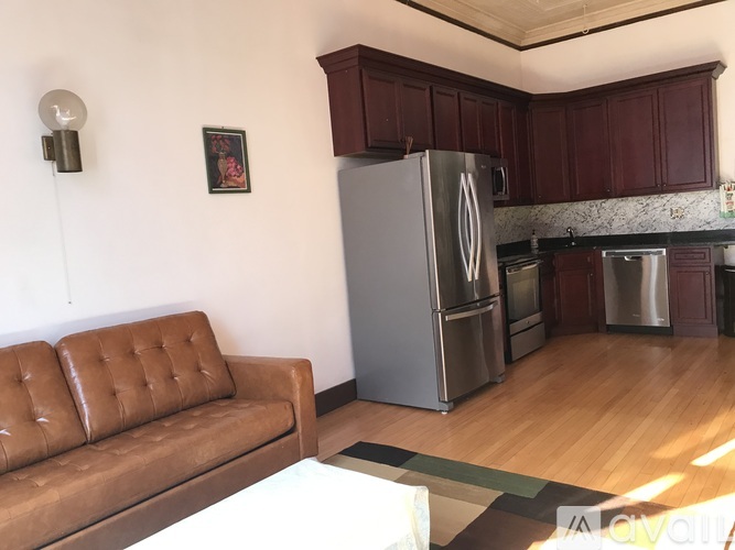 A brown leather couch sits in a kitchen with a refrigerator and stainless steel appliances.