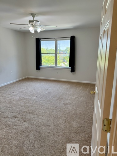 A room with a carpeted floor, a ceiling fan, and a window with black blinds.