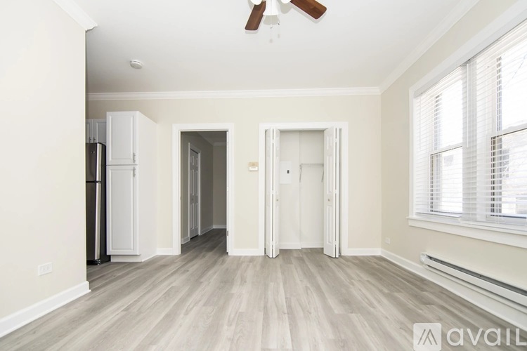A spacious room with a ceiling fan and light, hardwood floors, and a window with blinds.