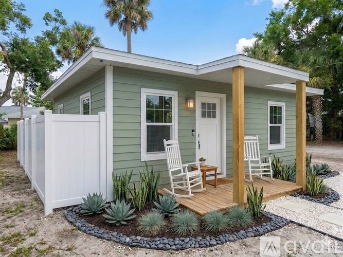 A small house with a porch and white chairs.
