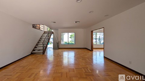 A spacious room with wooden flooring and a staircase leading to another level.