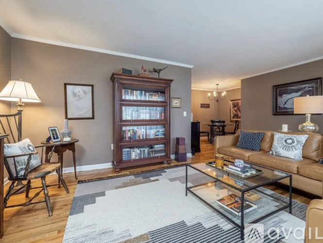 A living room with a brown couch, a glass coffee table, and a bookshelf filled with books.