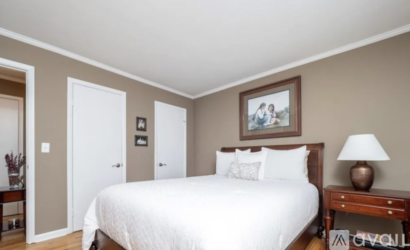 A bedroom with a large bed, a nightstand with a lamp, and a painting on the wall.