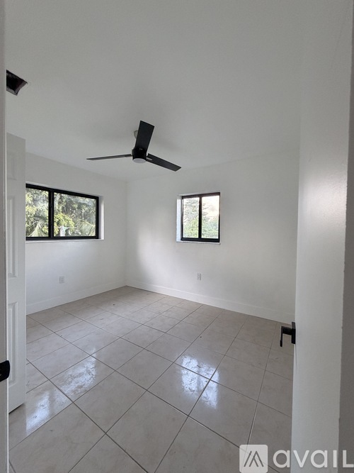 A room with a ceiling fan and two windows.