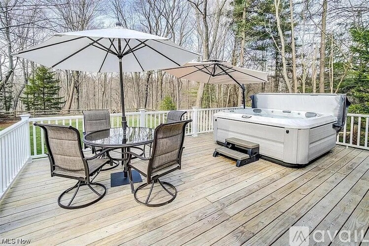 A hot tub sits on a wooden deck with chairs and an umbrella.
