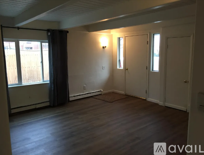A room with wooden floors and white walls, featuring a window with a black curtain and a white door.