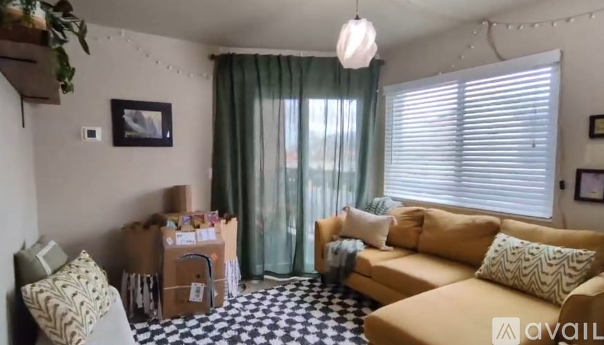A living room with a tan couch, a black and white checkered floor, and a window with green curtains.