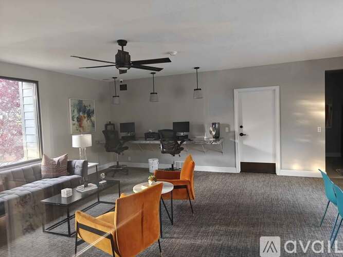 A living room with a grey carpet and a ceiling fan.