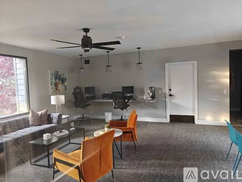 A living room with a grey carpet and a ceiling fan.