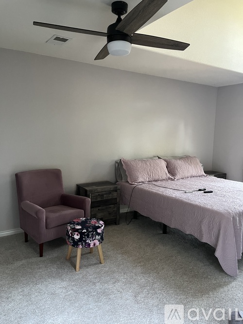 A bedroom with a bed, chair, and ceiling fan.