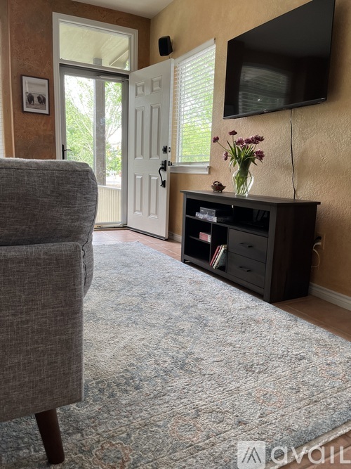 A grey sofa sits in a living room with a flat screen TV mounted on the wall.