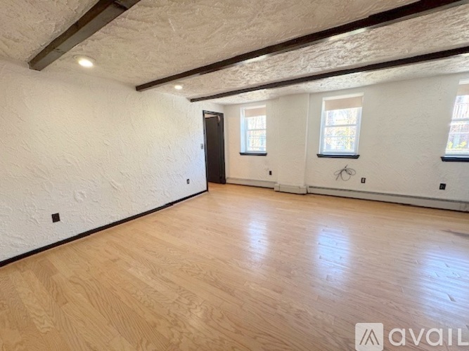 A room with wooden flooring and white walls, with a door on the left and two windows on the right.