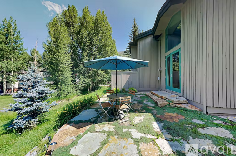 A patio with a chair and umbrella is surrounded by a grassy area and trees.
