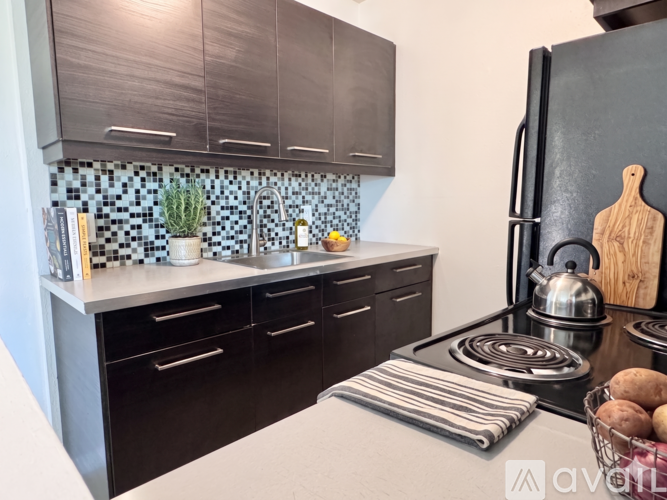 A kitchen with a black refrigerator, a stove, and a counter with a cutting board on it.