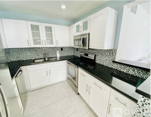A kitchen with white cabinets and black countertops.