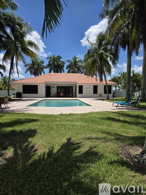 A house with a red roof and a pool surrounded by palm trees.