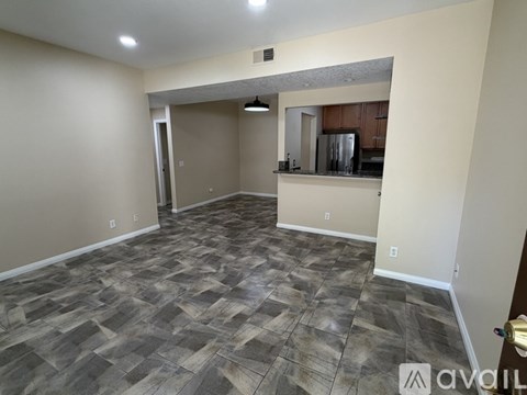 A room with a tiled floor and a kitchen area in the background.