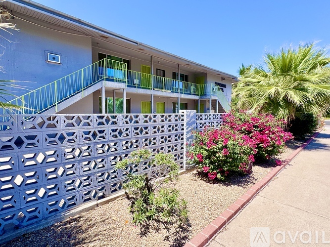 A blue building with a white lattice fence and a small garden with pink flowers.