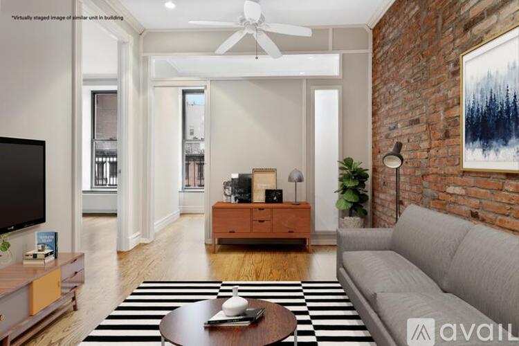 A living room with a grey couch, a coffee table, a television, and a brick wall.