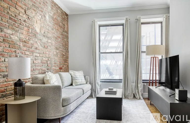 A living room with a grey couch, a white table, and a brick wall.