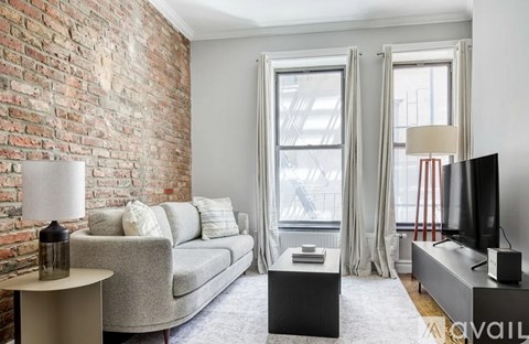 A living room with a grey couch, a white table, and a brick wall.