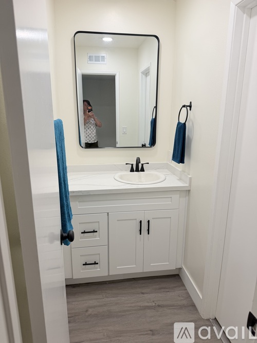 A person is taking a picture in a bathroom with a sink, mirror, and cabinets.