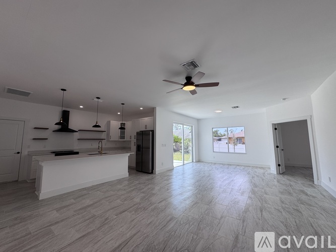 A spacious, empty room with a ceiling fan and a kitchen area with white cabinets and a countertop.