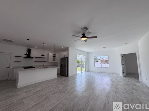 A spacious, empty room with a ceiling fan and a kitchen area with white cabinets and a countertop.