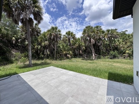 A concrete patio with a white wall and palm trees in the background.