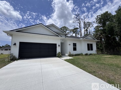 A white house with a black garage door is surrounded by greenery.
