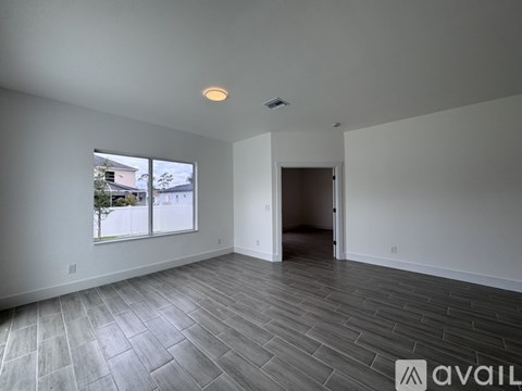 A spacious room with a large window and a door leading to another room.