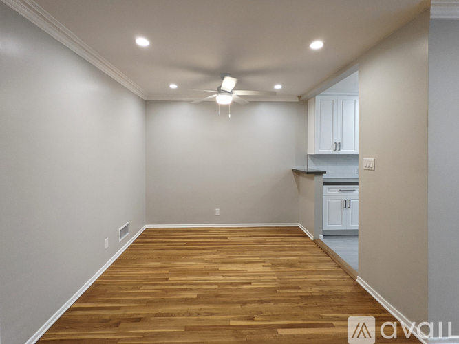 A spacious room with wooden flooring and a kitchen area in the background.