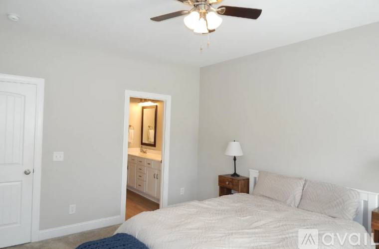 A bedroom with a bed, a ceiling fan, and a nightstand with a lamp.
