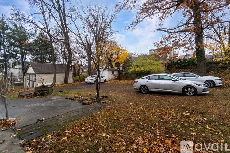 A silver car is parked in a driveway with a house and trees in the background.