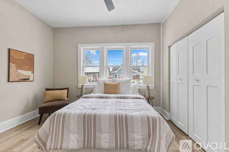 A bedroom with a large bed and a view of a residential area through the windows.