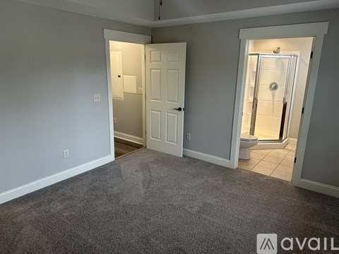 A room with a carpeted floor and two doors, one of which opens to a bathroom.