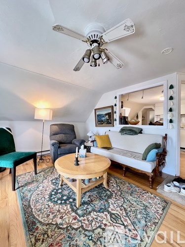 A living room with a rug, a sofa, a chair, a coffee table and a ceiling fan.