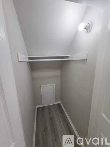 A white hallway with a clock on the wall and a shelf above a door.