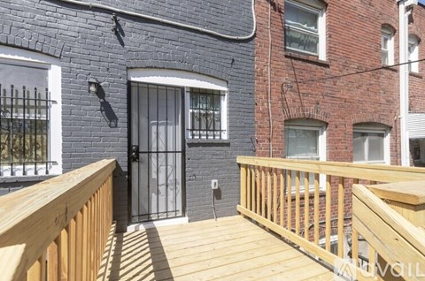 A wooden deck leads to a black door on a brick building.